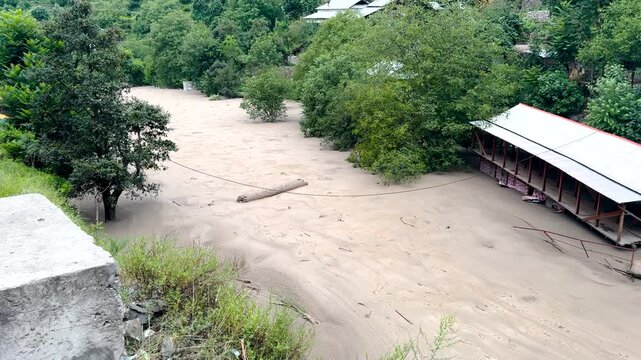 Raging muddy river torrent overflowing banks and threatening riverside structures during a severe monsoon flash flood in Katha Piran, Pakistan