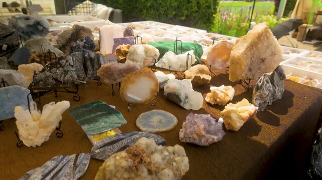 A variety of authentic raw minerals, quartz crystals, and polished gemstones displayed on a table at an outdoor market. Useful for wellness, geology, and alternative medicine content.