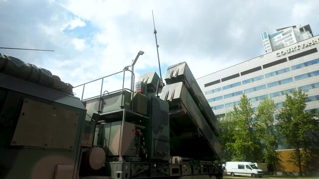 A camouflage mobile missile defense system parked near a modern hotel building in Gdynia, Poland. Suitable for news, defense, and geopolitical content.