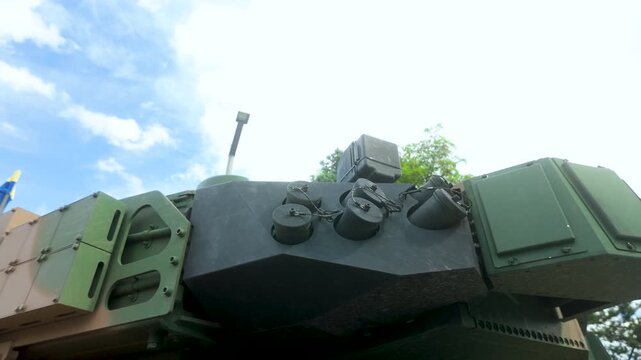Low angle view of a modern main battle tank turret featuring reactive armor and smoke grenade launchers under a blue sky. Suitable for defense, security, and military technology content.