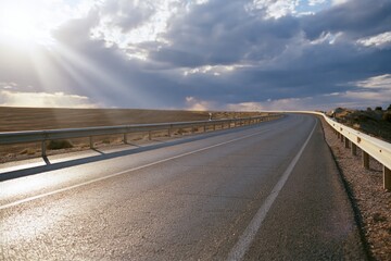 Obraz premium The Road Under Sunlit Sky: Serene Desert Highway Stretch at Dusk