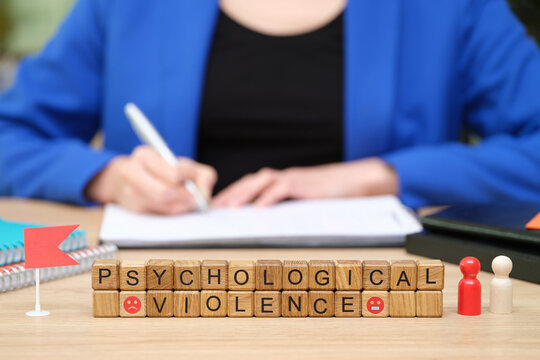 In a quiet workspace, a thoughtful individual writes notes while symbolic blocks spell out 'Psychological Violence.' The setting encourages reflection and dialogue about mental health.