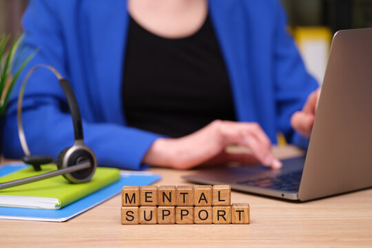In a bright and inviting workspace, a person types on a laptop while focusing on mental support materials. Headphones rest nearby, showcasing the importance of online communication.