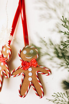 Gingerbread Christmas ornaments hang on red ribbons near green foliage during the holiday season