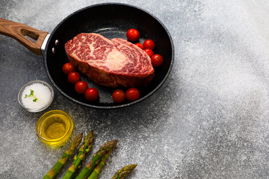 Cooking steak with cherry tomatoes and asparagus in a frying pan on a gray background