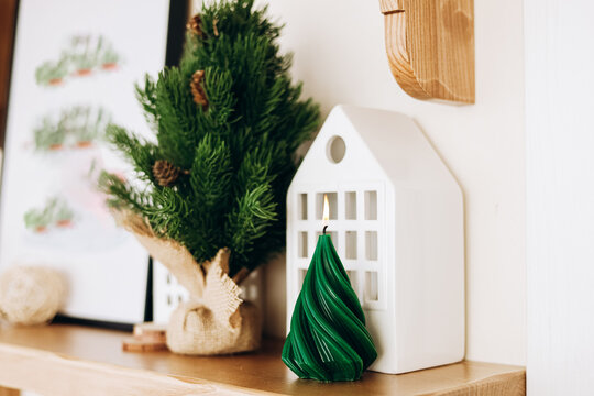 Decorative green Christmas candle and small tree placed on a shelf with art and decor in a cozy indoor space during winter