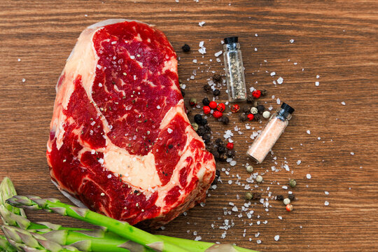 Steak placed on wooden table with spices and asparagus ready for cooking