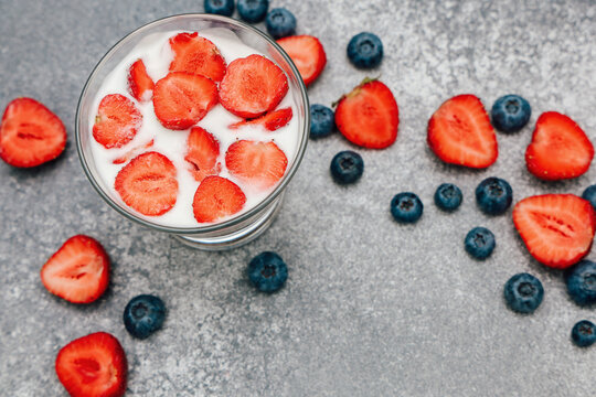 Fresh strawberries and blueberries with yogurt in a glass on a gray surface