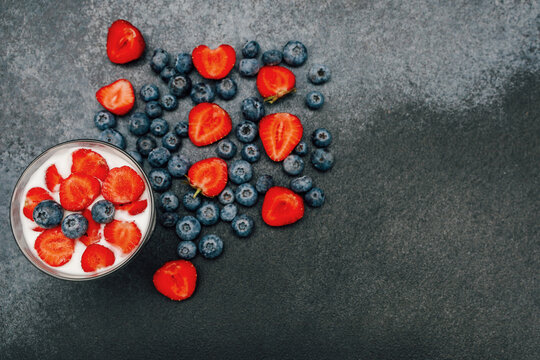 Mix of strawberries and blueberries on dark background with yogurt in glass