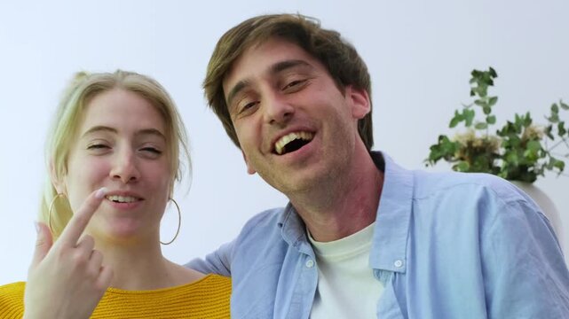 A happy young couple laughs hysterically while watching amusing content on a smartphone at home, sharing a joyful moment and connecting over digital entertainment.