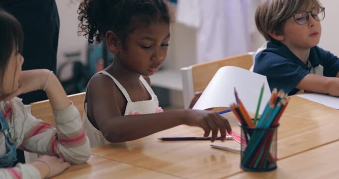Teacher handing out white paper to diverse elementary students sitting at classroom desks.