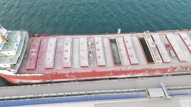 An aerial drone shot shifts right over the open blue water, tracking across the bridge superstructure and expansive red cargo hold doors of the docked vessel CSL Tadoussac