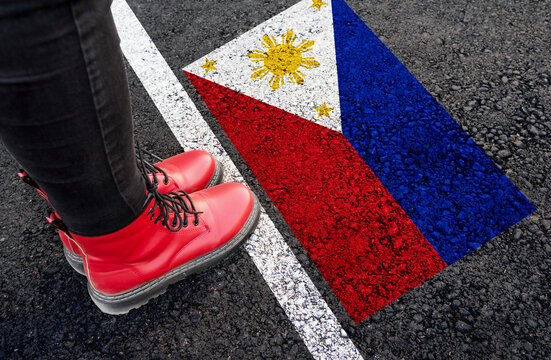 a woman with a boots standing on asphalt next to flag of Philippines and border
