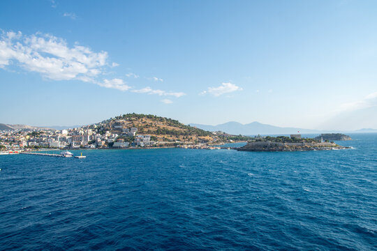 View of a coastal town with a historic castle on a small island, harbor, and blue sea under a clear sky in Selcuk, Izmir, Turkiye.