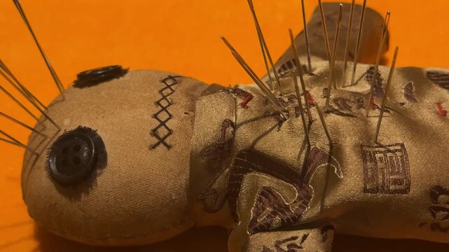 Voodoo doll made of fabric with needles stuck in it. Traditional mystical object for magic ritual. Dark occult theme and spiritual symbol on orange background.