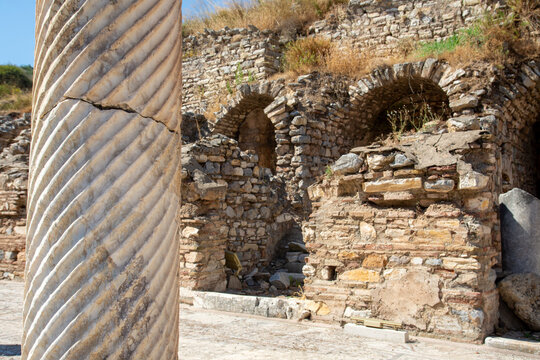 View of a fluted marble column standing before the ancient stone ruins and arched structures of Ephesus Ancient City in Selcuk, Izmir, Turkiye.