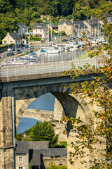 Naklejka premium Multi-layered scenic view of the massive stone arch viaduct in Dinan, France, framing a historic river bridge, traditional houses, and the port with sailboats.