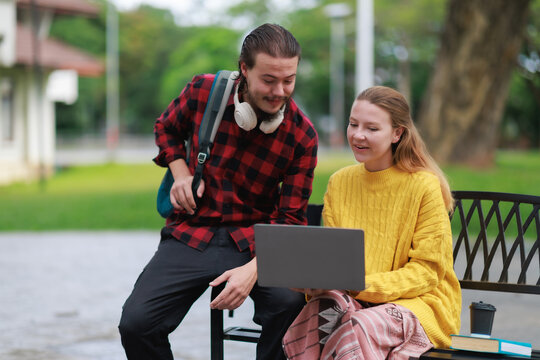 University students collaborating on laptop outdoors, discussing project on campus, learning together, studying modern technology, sharing ideas, enjoying college life