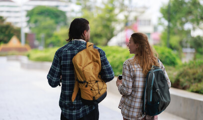 Fototapeta premium Two friends or a couple wearing plaid shirts and backpacks walking away from the camera, engaging in conversation while exploring an urban environment