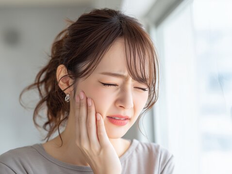 歯の痛みや知覚過敏に悩み頬を抑えて顔をしかめる虫歯や歯周病の疑いがある茶髪の女性