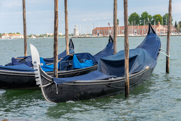 Covered Venetian gondolas moored by wooden poles on lagoon waterfront © Anton