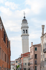 Fototapeta premium Tall white campanile rising above narrow Venetian street under cloudy sky