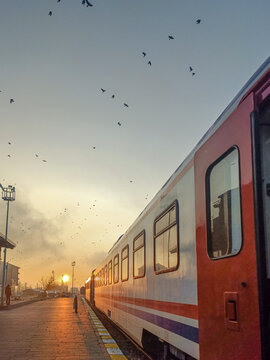 View of the Eastern Express train parked at the station in Kars during a golden sunset with birds flying in the sky, Kars, Kars, Turkiye.