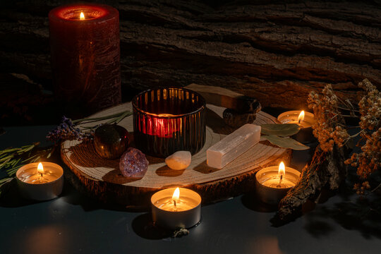 Mystical witchcraft altar with a burning tealight candle surrounded by lavender, rosemary, amethyst crystal, black obsidian, and volcanic stone arranged on a rustic wooden log slice, evoking magic