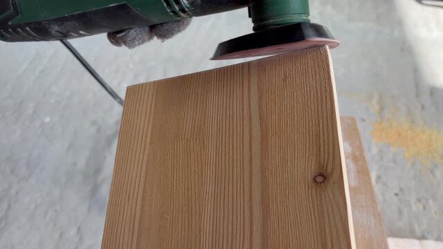 the process of carpentry, woodworking, or home renovation in a sunlit workshop. A worker sanding the edge of a wooden board