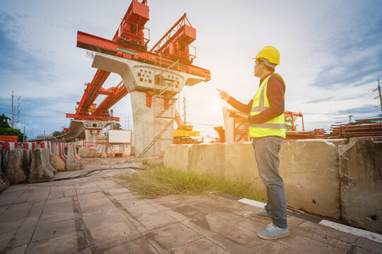 Asian foreman is writing a work summary on a tablet, digitizing the information before leaving work on a construction site for a new concrete road and bridge a critical infrastructure project.