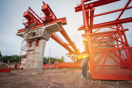 Asian civil engineers use tablets to record electronic data at a concrete highway bridge construction site. A male supervisor is inspecting things at the new concrete road and bridge construction site