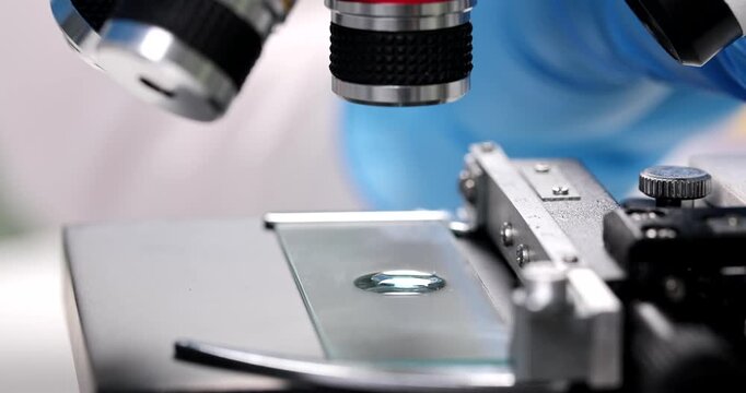 Bright blue gloves carefully adjust the lens of a microscope, illuminating a slide with precision. A captivating journey into the unseen world begins as the focus sharpens.