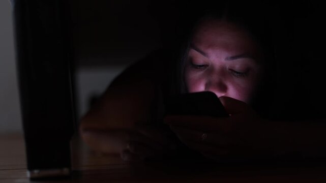 Domestic violence victim hides beneath bed and calls police for protection. Emergency lights illuminate her face while she waits for help.