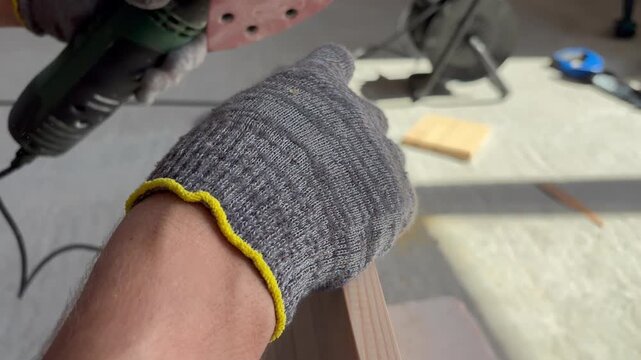 Man's hands using a green delta sander for woodworking on a pine board. DIY furniture making and carpentry concept.