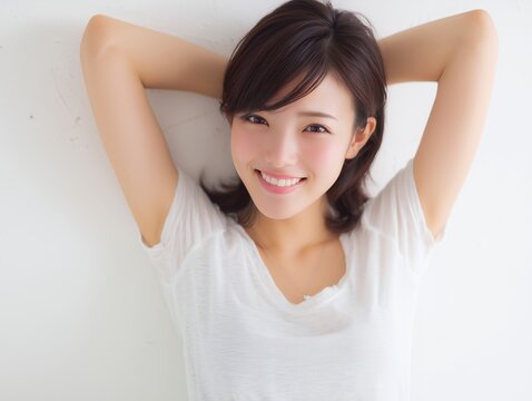 白いTシャツを着てリラックスした表情で両手を頭の後ろに添えて微笑む笑顔の女性