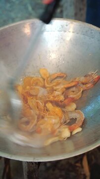 Cooking Thai stir-fried lotus shoots with fresh prawns. Sauteing crushed garlic and whole prawns in a hot wok, seasoning with sauces, adding fresh bite-sized lotus shoots (lai bua), and stir-frying ov