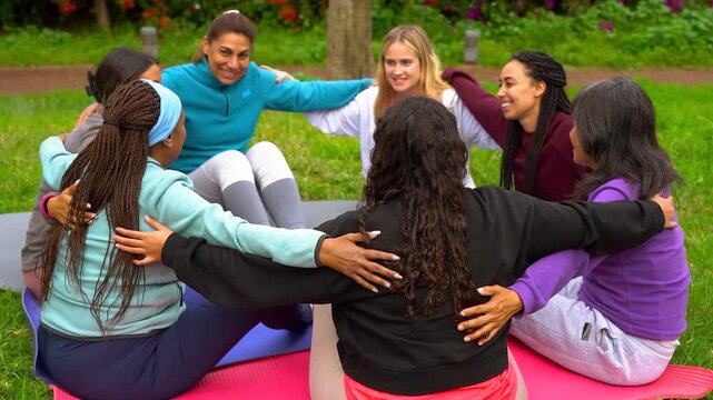 Multiracial women circle hugging each other while doing group meditation at city park - Multi generational people, healing and connection concept