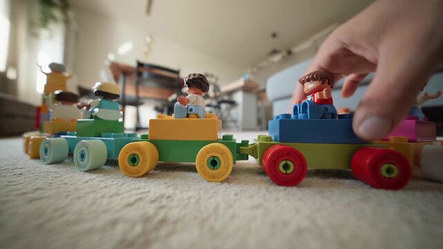 Adult hand placing a toy figure onto a colorful building block train on a carpet, low angle close up of imaginative play, early learning and family time at home