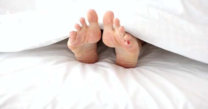 Under a soft blanket, a pair of feet playfully peek out, adorned with bright red nail polish. Gentle light filters in, creating a peaceful morning vibe filled with comfort and contentment.