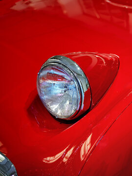 Detailed view of the front corner of a red classic car, highlighting its round headlight.