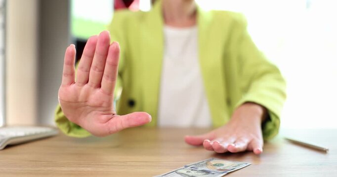 In a well-lit cafe, a woman in a stylish lime green jacket demonstrates the art of saying no with calm gestures. Her hands convey confidence and poise as she rejects an offer gracefully.