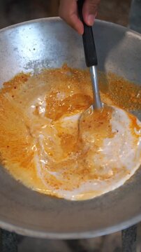 Cooking Thai red curry with chicken and pickled bamboo shoots. Stir-frying red curry paste with coconut milk in a wok, adding sliced chicken and pickled bamboo slices, transferring to a pot with cocon