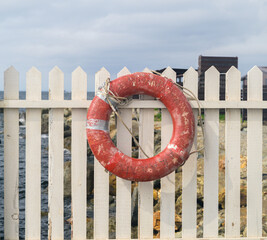 Weathered red lifebuoy hanging on wooden fence. © Vladimir Arndt