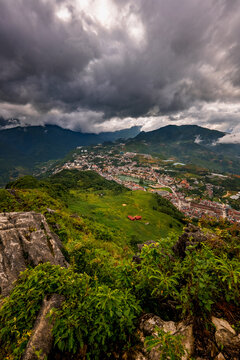 View of Sa Pa town nestled in the lush green mountains of the Hoang Lien Son range under a dramatic cloudy sky in Sa Pa, Lao Cai, Vietnam.