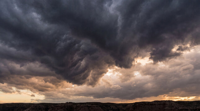 Intense and textured dark storm clouds loom dramatically over an arid desert landscape at sunset.