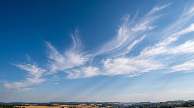 Panoramic photograph of a vibrant blue sky with elegant cirrus clouds over a rolling green landscape.
