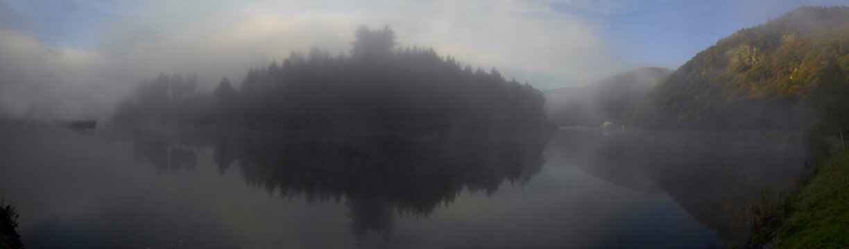 Blick vom Leinpfad unten am Flu&szlig; auf die Saarschleife im Morgennebel mit Binnenschiff, das aus dem Nebel auftaucht.