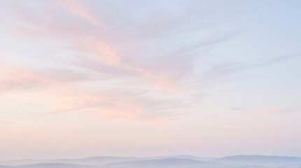 Fototapeta premium Expansive pastel sky with soft pink and blue hues, adorned with wispy clouds above hazy, distant mountains.