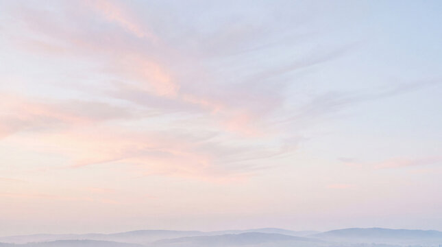 Expansive pastel sky with soft pink and blue hues, adorned with wispy clouds above hazy, distant mountains.