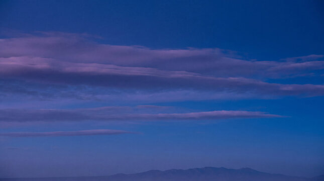 Beautiful twilight sky with long, wispy purple clouds above distant, hazy mountain silhouettes.